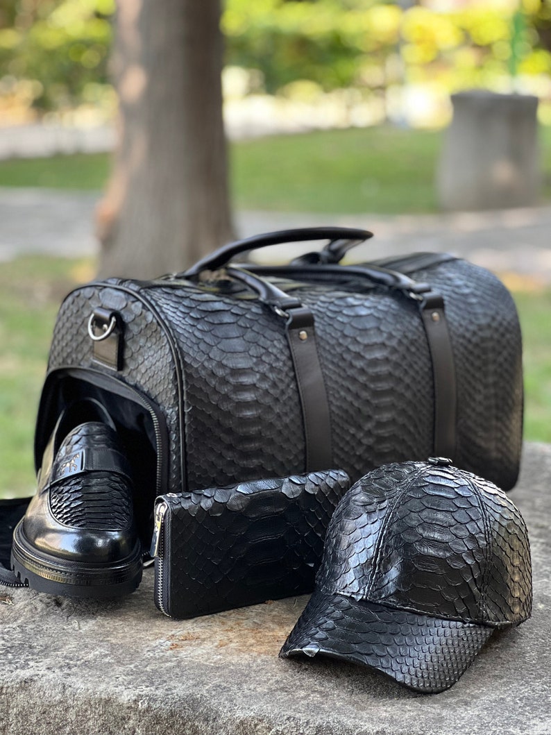 Pode incluir: Um conjunto de acess&oacute;rios em couro preto com textura de pele de cobra. Inclui uma mala de viagem, mocassins, uma carteira e um bon&eacute; de beisebol. A mala tem uma al&ccedil;a superior e uma al&ccedil;a de ombro.