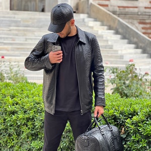 Pode incluir: Casaco, bon&eacute; de beisebol e mala de viagem em couro preto. O casaco tem um padr&atilde;o texturizado, fecho de correr e gola. O bon&eacute; &eacute; de estilo beisebol cl&aacute;ssico. A mala de viagem tem uma textura correspondente e uma pega superior.