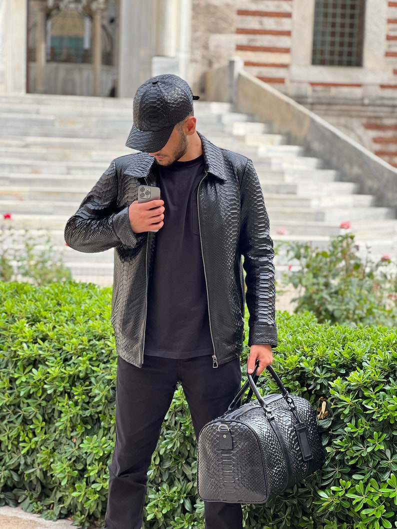 Pode incluir: Casaco, bon&eacute; de beisebol e mala de viagem em couro preto. O casaco tem um padr&atilde;o texturizado, fecho de correr e gola. O bon&eacute; &eacute; de estilo beisebol cl&aacute;ssico. A mala de viagem tem uma textura correspondente e uma pega superior.