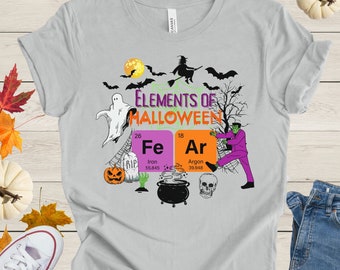 May include: A gray t-shirt with a Halloween themed design featuring a witch, ghost, pumpkin, cauldron, and skull. The design includes the text "Elements of Halloween" and the chemical symbols for iron (Fe) and argon (Ar).