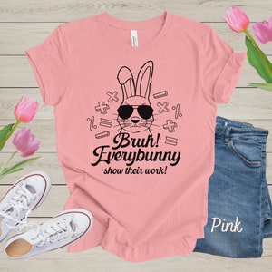 May include: Pink t-shirt with a black and white illustration of a bunny wearing sunglasses and surrounded by math symbols. The text "Bruh! Everybunny show their work!" is printed on the shirt.