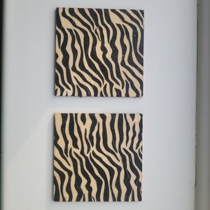 May include: Two square wall decorations featuring a black and beige zebra stripe pattern.