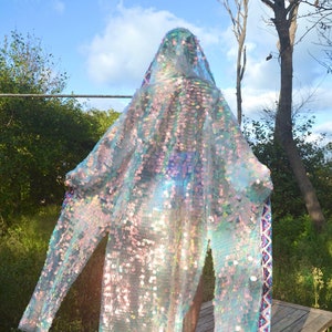 May include: A long, iridescent, sequined robe with a hood. The robe has a colorful trim along the edges. The robe is worn by a person standing on a wooden platform.