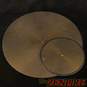 May include: Two black circular mats with concentric gold lines radiating from the center. The mats are different sizes, with the larger one in the background. The text "The ZENPIRE" is at the bottom right.