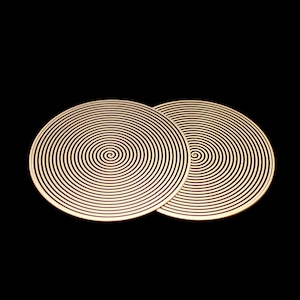 May include: Two circular coasters with a spiral design. The coasters are beige with black lines, creating a hypnotic pattern. The background is solid black.