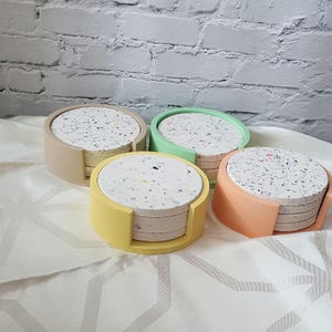 May include: Set of four round coasters with a terrazzo pattern. The coasters are made of a light beige, light green, light yellow, and light orange material.