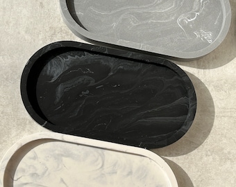 May include: Three oval-shaped trays arranged vertically. The top tray is gray with white marbling, the middle tray is black with subtle dark gray swirls, and the bottom tray is white with light gray marbling. Each tray has a raised edge.