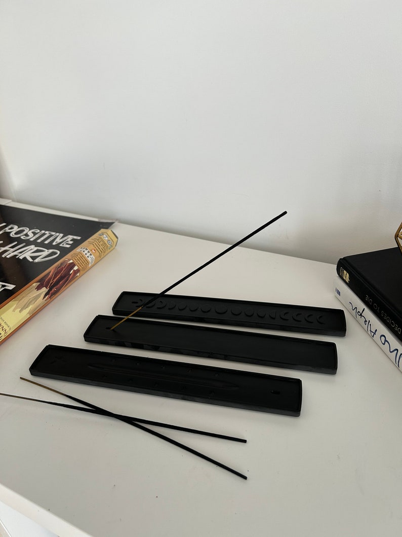 May include: Three black incense holders with a row of small circles on the top. Two black incense sticks are laying on top of the holders.