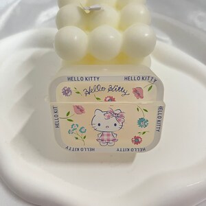 May include: A white Hello Kitty candle with a bubble design. The candle has a Hello Kitty graphic on the front with flowers and the text "Hello Kitty" repeated around the border.