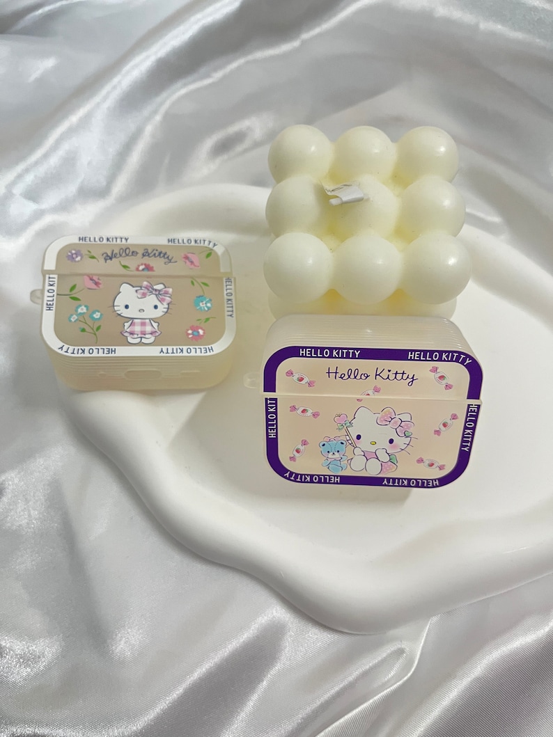 May include: Two Hello Kitty themed candle holders. One is a square with a white Hello Kitty design and the other is a white cube with round bumps.
