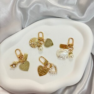 Op de afbeelding: Vier gouden sleutelhangers met verschillende bedels. Elke sleutelhanger heeft een hartbedel met de woorden "The Ocean is my happy place" en een parel accent. De bedels omvatten een schelp, een parelhart en een enkele parel.