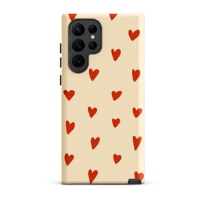 May include: A cream-coloured phone case with a repeating pattern of red hearts. The case has a cutout for the phone's camera lens.