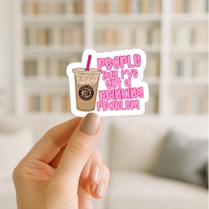 May include: A die-cut sticker featuring a light brown iced coffee in a plastic cup with a pink straw and ice cubes. The text in pink bubble letters reads: People say I've got a drinking problem. The cup features a circular Seven Brew logo.
