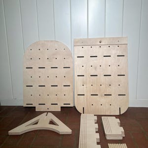 May include: A set of unfinished wooden pieces for building a jewellery organiser. The set includes two large panels with holes, a triangular base, and several smaller pieces for shelves and dowels.