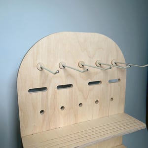 May include: A wooden jewelry organizer with two shelves and hooks. The organizer is made of light wood and has a rounded top.