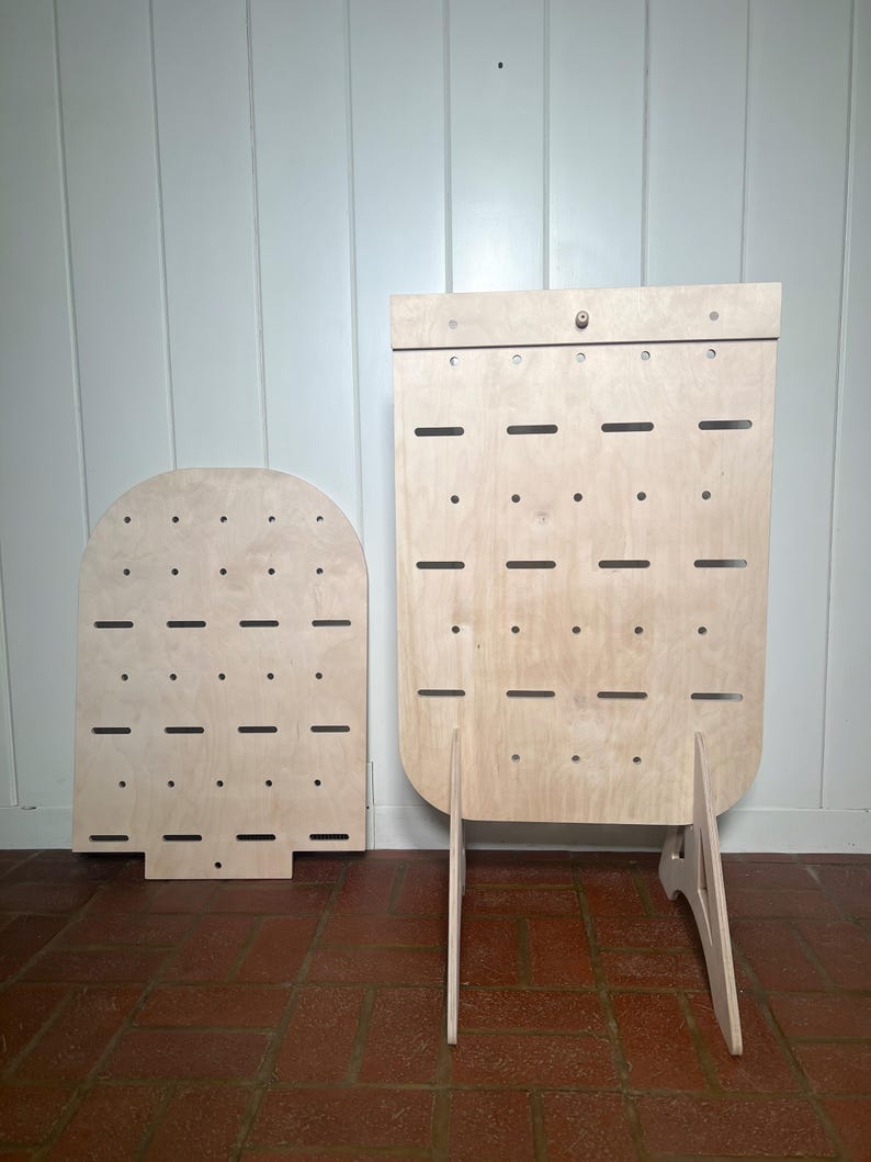 May include: Two wooden earring display stands with multiple holes for hanging earrings. The larger stand has a triangular base and the smaller stand is free-standing.