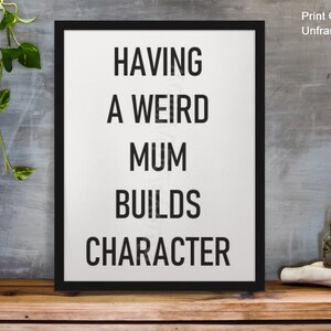 May include: Black and white typography print with the text "Having a weird mum builds character" on a white background in a black frame.