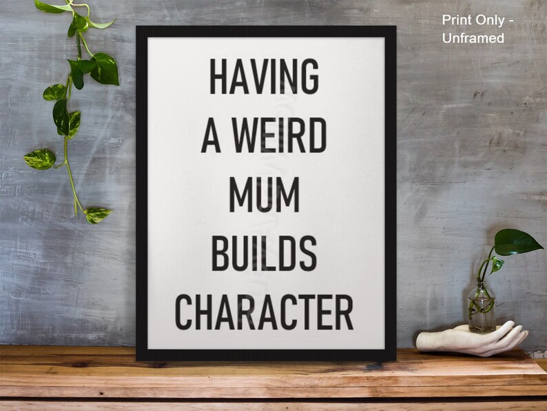 May include: Black and white typography print with the text "Having a weird mum builds character" on a white background in a black frame.