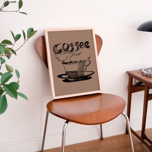 May include: A framed print of a black and white illustration of a coffee cup with steam rising from it. The word "Coffee" is written in a stylized font above the cup.