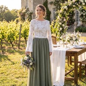 Può includere: Un abito da sposa con un top in pizzo bianco e una gonna verde. La donna tiene in mano un bouquet di fiori bianchi e viola. Un tavolo è apparecchiato per un ricevimento di nozze con composizioni floreali e candele.