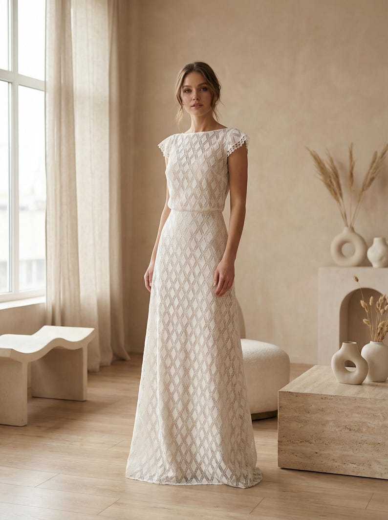 May include: A floor-length ivory dress featuring a repeating diamond pattern throughout the fabric, a boat neckline, and short cap sleeves with a delicate scalloped edge. The garment has a fitted bodice and a long, straight skirt silhouette.