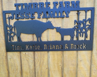 以下が含まれることがあります： 「Timbre Farm Jesse Family Tim, Katie, Briana & Breck」という文字と、トウモロコシ畑に立つ2頭の牛のシルエットが描かれた黒い金属製の看板です。