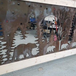 Puede incluir: Una pieza de arte rústica de metal que representa una escena de bosque con osos, árboles y estrellas. La obra de arte está cortada de metal y montada sobre un marco de madera. Los osos y los árboles son siluetas.