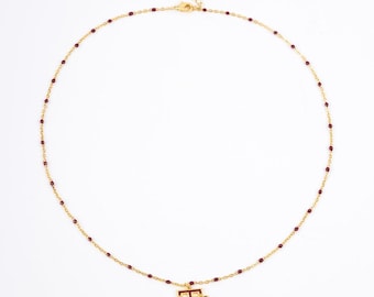 May include: Gold chain necklace with maroon beads and a gold pendant featuring the letters "A" and "M" on either side of a gold "T".