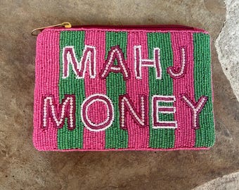 May include: A rectangular zippered pouch featuring vertical stripes of pink and green glass beads. The text "MAHJ MONEY" is embroidered in white beads with a pink outline across the centre of the pouch. A gold-toned metal zipper pull is visible.