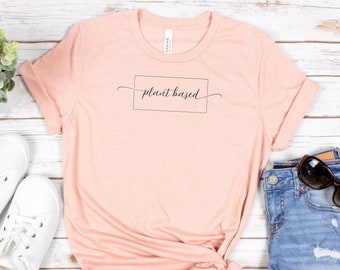 May include: A light pink t-shirt with the text "plant based" in a black box and a cursive font.