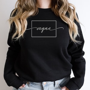 Könnte beinhalten: Schwarzer Pullover mit einem weißen Quadrat und dem Wort "vegan" in Kursivschrift im Quadrat.
