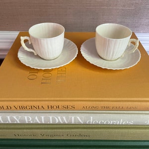 Puede incluir: Dos tazas de té blancas y platillos con un diseño acanalado. Las tazas tienen un asa curva delicada. Los platillos tienen un borde festoneado.