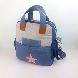 Könnte beinhalten: Ein blauer und grauer Canvas-Rucksack mit einem roten und weißen Sternmuster. Der Rucksack hat einen Tragegriff oben und einen Schultergurt. Er hat auch eine vordere Tasche mit einem Reißverschluss.