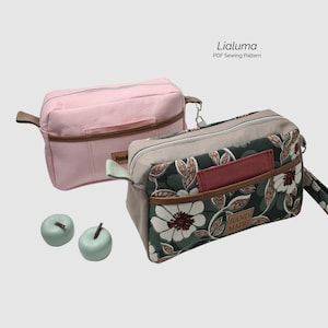 Könnte beinhalten: Zwei Stoff-Reißverschlusstaschen, eine rosa und eine mit Blumendruck. Die Blumentasche hat einen braunen Ledereinsatz und den Text "HAND MADE".