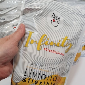May include: A white bag with a yellow and black logo that says "Infinity #CreaSinLímites" and "Masa de Porcelana Liviana & flexible". The bag has a white and grey striped pattern. The bag is labelled with a 325g weight.