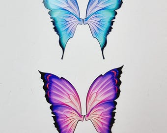 Op de afbeelding: Twee sets vlindervleugels worden afgebeeld. De ene set is blauw en turquoise, de andere paars en roze. De vleugels hebben gedetailleerde aderpatronen en zwarte omtrekken. Ze zijn waarschijnlijk bedoeld voor kostuums of knutselwerk.