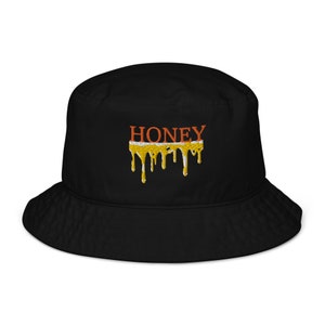 May include: Black bucket hat with the word "HONEY" embroidered in orange and a dripping honey design in yellow and orange.