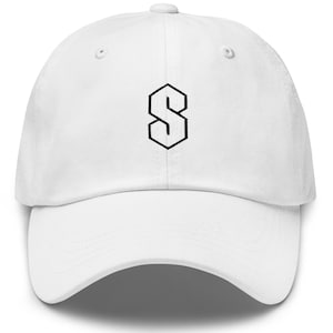 Puede incluir: Gorra de béisbol blanca con un contorno negro de la letra "S" en la parte delantera. La gorra tiene una visera curva y una correa ajustable en la parte trasera. Hecha de un material suave y duradero.