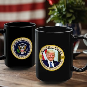 May include: Two black ceramic mugs with a white background. One mug features the Presidential Seal of the United States. The other mug features a portrait of Donald J. Trump with the text "45 PRESIDENT OF THE UNITED STATES 47".