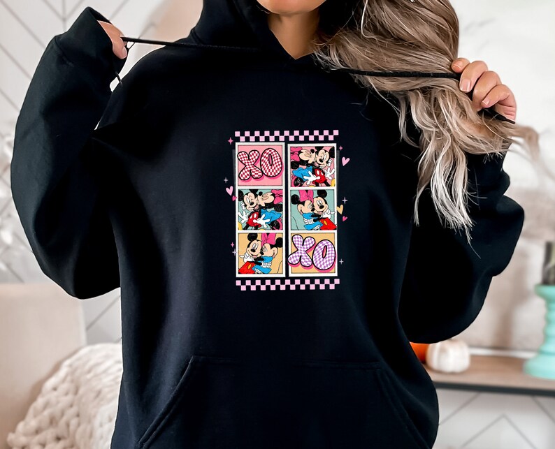 May include: Black hoodie featuring a colorful graphic of Mickey and Minnie Mouse in various romantic poses. The design includes the letters "XO" and a pink and white checkered border. The hoodie has a drawstring hood and a front pocket.