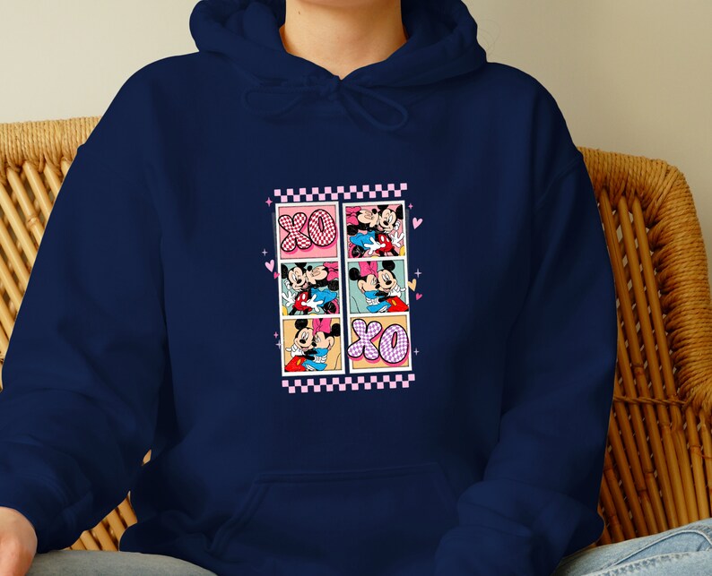 May include: Navy blue hoodie featuring a graphic of Mickey and Minnie Mouse in a comic strip style. The design includes the letters "XO" and pink and black checkered borders. The hoodie is made of a soft material.
