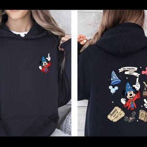 Op de afbeelding: Marineblauwe hoodie met een kleine geborduurde Mickey Mouse als tovenaar op de voorkant. De achterkant toont een kleurrijke afbeelding met Mickey, een tovenaars hoed en de tekst "Some imagination, Huh?" Een leuk, grillig ontwerp.