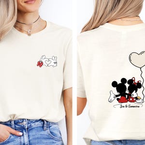 May include: Cream-coloured t-shirt with a cartoon design. The front shows a white bunny with a red bow and a heart. The back features Mickey and Minnie Mouse with a heart-shaped balloon and the names "Joe & Samantha".