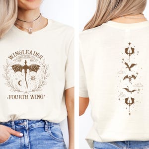 May include: A white t-shirt with a brown graphic of a dragon and the text "WINGLEADER RIDERS SQUADRAST FOURTH WING". The back of the shirt has a vertical design of five dragons with stars and clouds.