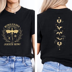 May include: Black t-shirt with a gold graphic of a dragon and the text "WINGLEADER FOURS GUARDIAN -FOURTH WING-". The back of the shirt has a vertical row of gold dragon silhouettes.