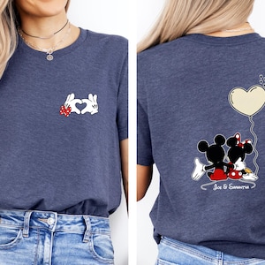 May include: A navy blue t-shirt with a Mickey Mouse and Minnie Mouse design. The front displays white gloved hands forming a heart with a red bow. The back shows Mickey and Minnie with a heart balloon and the names "Joe & Samantha".