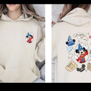 Op de afbeelding: Beige hoodie met een Mickey Mouse cartoon ontwerp. De voorkant heeft een kleine Mickey Mouse afbeelding in een tovenaarsoutfit. De achterkant toont een groter ontwerp met Mickey, een tovenaars hoed en de tekst "Some imagination, Huh?"