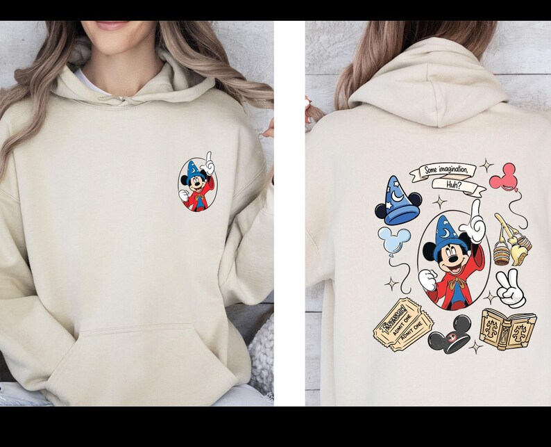 Op de afbeelding: Beige hoodie met een Mickey Mouse cartoon ontwerp. De voorkant heeft een kleine Mickey Mouse afbeelding in een tovenaarsoutfit. De achterkant toont een groter ontwerp met Mickey, een tovenaars hoed en de tekst "Some imagination, Huh?"