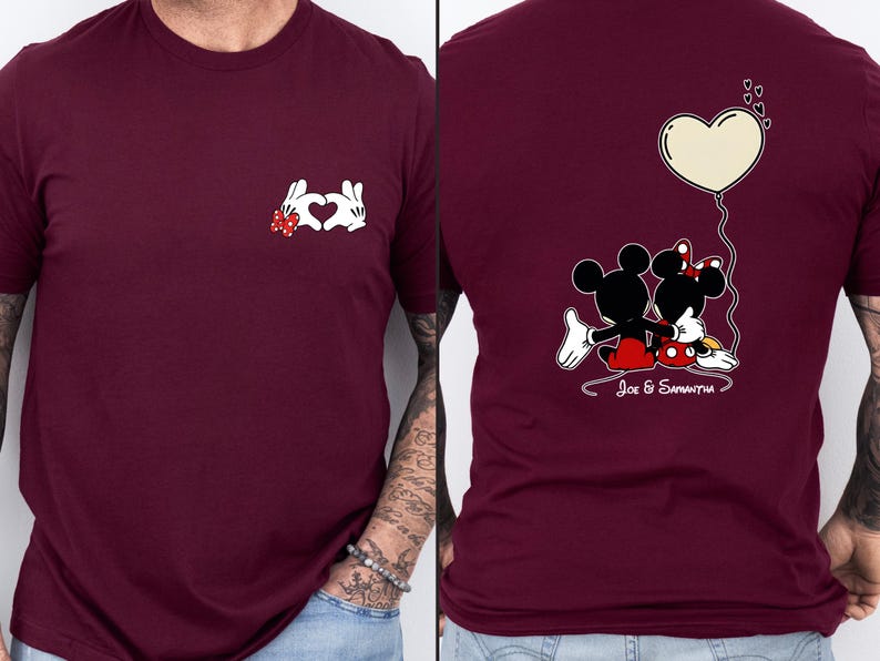 May include: Burgundy t-shirt with a white hand-heart design and a red bow. The back of the shirt shows a cartoon couple with a heart-shaped balloon and the text "Joe & Samantha".