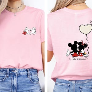 May include: Pale pink t-shirt with a cartoon rabbit design and a heart on the front. The back of the shirt features Mickey and Minnie Mouse with a heart-shaped balloon. The names "Joe & Samantha" are printed below the characters.
